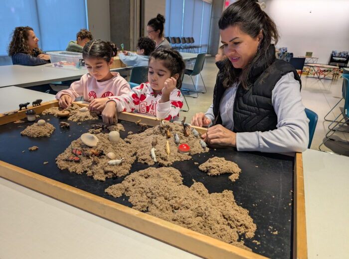 Two children and an adult play with kinetic sand while sitting at a table.